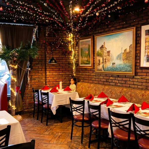 Cozy restaurant interior with brick walls, framed art, white tablecloths, red napkins, and a young girl seated.