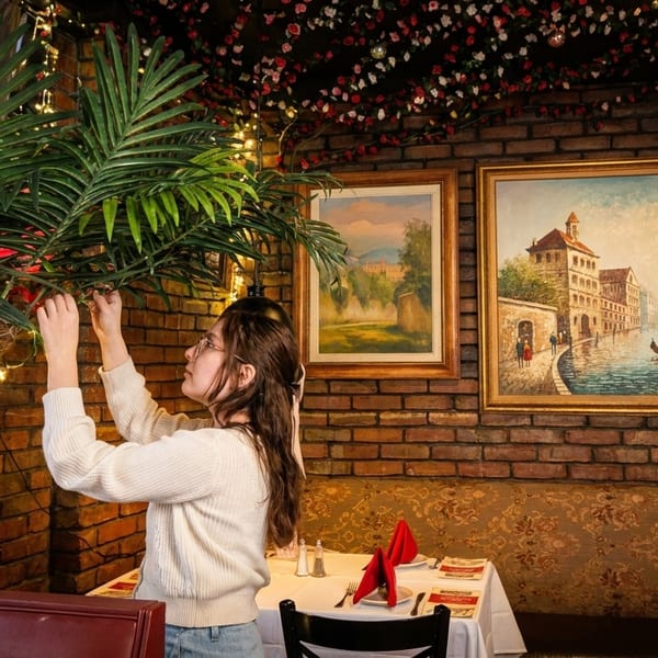 Woman decorating a palm tree with string lights in a restaurant with brick walls and paintings.