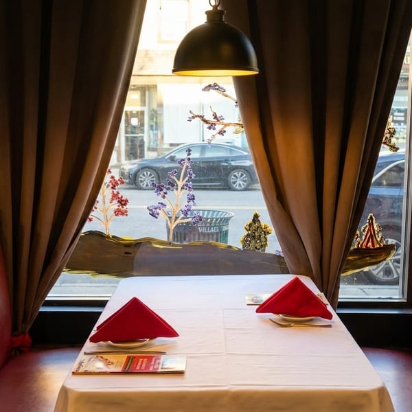 Cozy restaurant booth with red seating, white tablecloth, red napkins, and a street view.