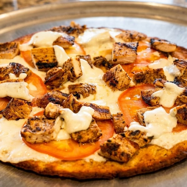 Grilled chicken and tomato pizza with white sauce on a metal tray.