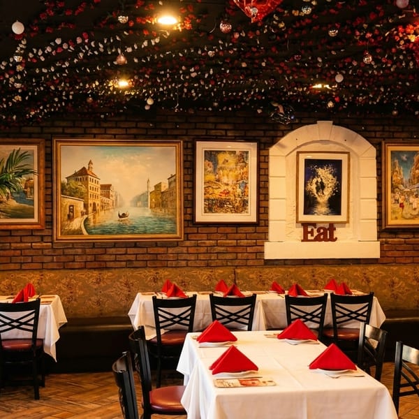 Cozy restaurant interior with brick walls, framed art, red booths, and tables set with white cloths and red napkins.